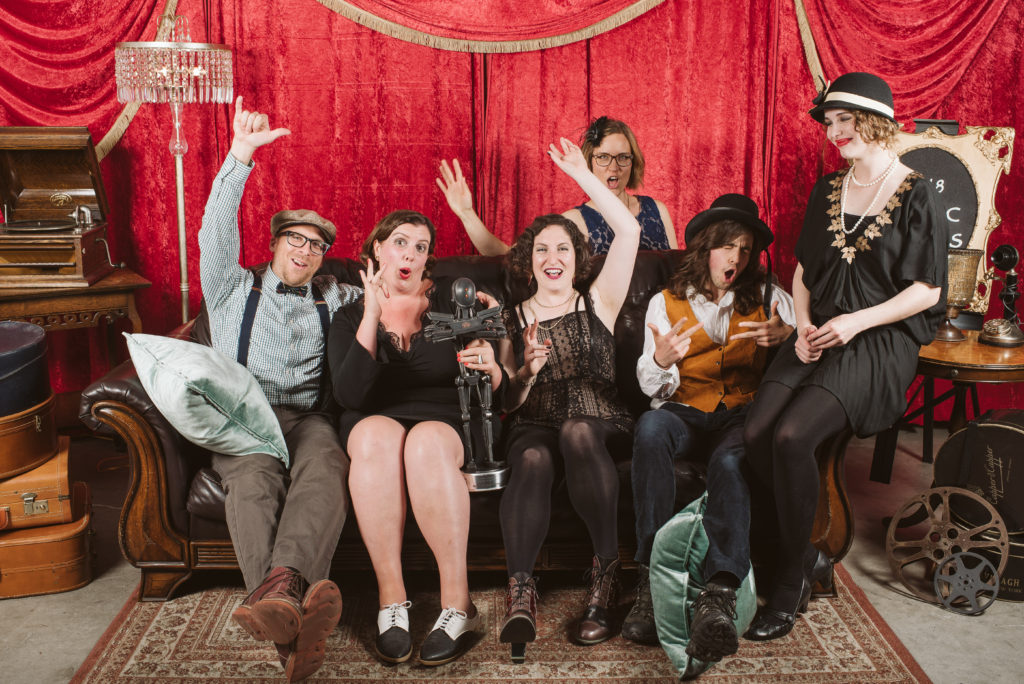 The AE team in 1920s-inspired dress, crowded onto a sofa in front of a red curtain backstage at the VIATEC Awards.