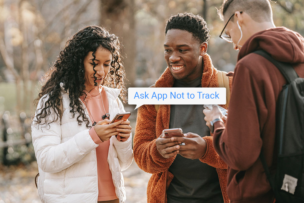 Three young adults standing in a semi circle, looking at their phones and smiling. A speech bubble is coming from one of the phones and says: "Ask App Not to Track"